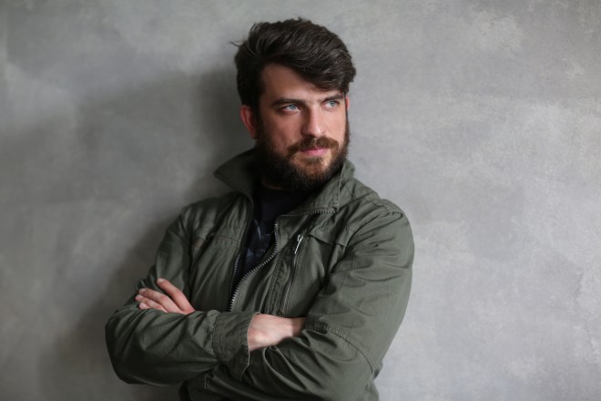 Guy in khaki jacket leaning on wall with crossed hands. Close.up. Black